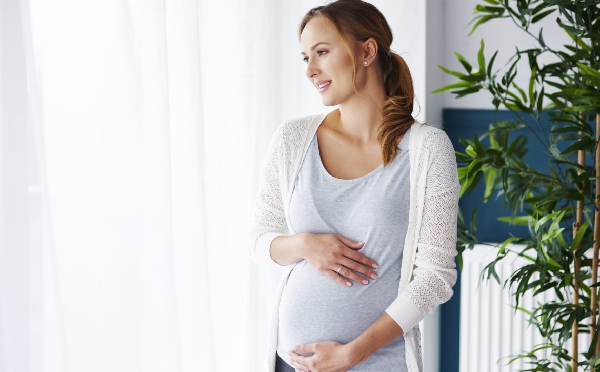 Cheerful pregnant woman looking through window