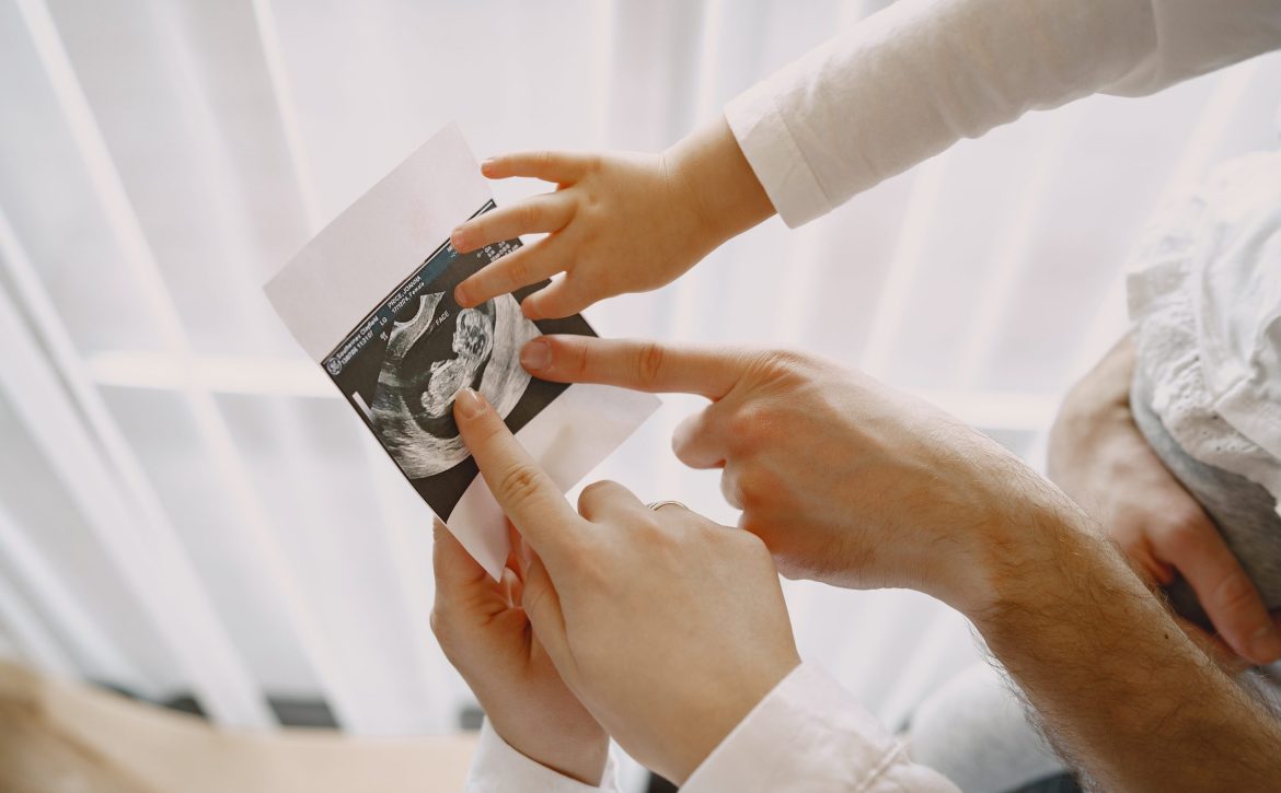 Pregnant mom dad and little daughter look at photo